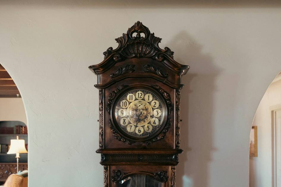 Founder posing beside an ornate mahogany grandfather clock in a cozy study filled with books and vintage decor