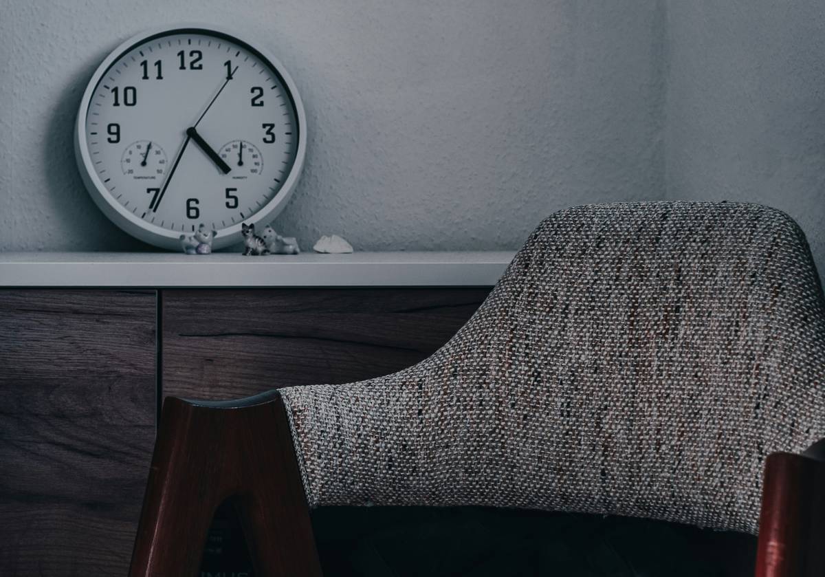 A brass-finished analog tabletop clock centered on a walnut console table with books and a ceramic vase, demonstrating ideal placement for tabletop clocks for living room decor